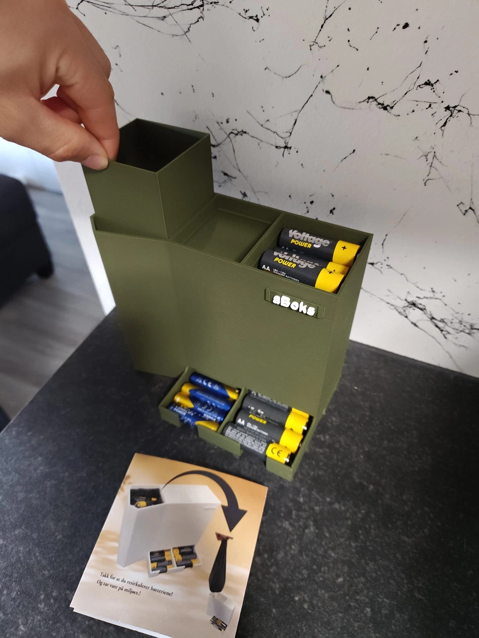 Olivengrønn aBoks i bruk på en kjøkkenbenk – modulen for brukte batterier løftes ut