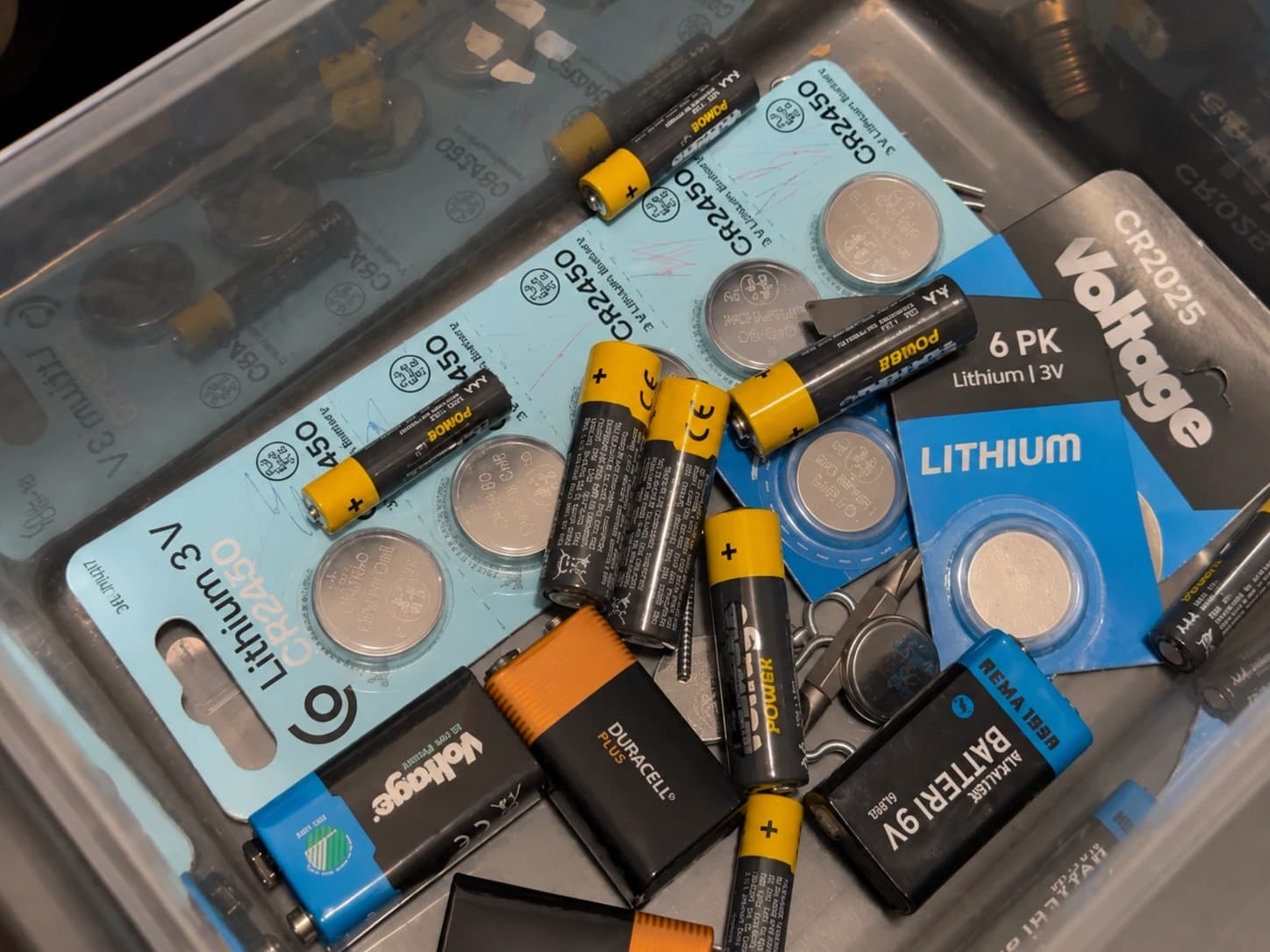 Løse AA-, AAA-, knappcelle- og 9V-batterier blandet med emballasje i en plastboks